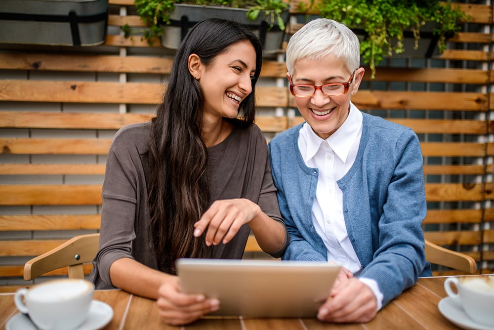 Using digital tablet. Two happy smiling women using digital tablet at a table