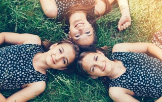 Three sisters lying down in the grass and smiling to the camera