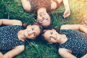 Three sisters lying down in the grass and smiling to the camera