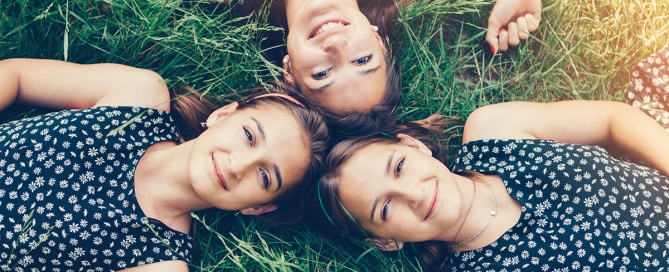 Three sisters lying down in the grass and smiling to the camera