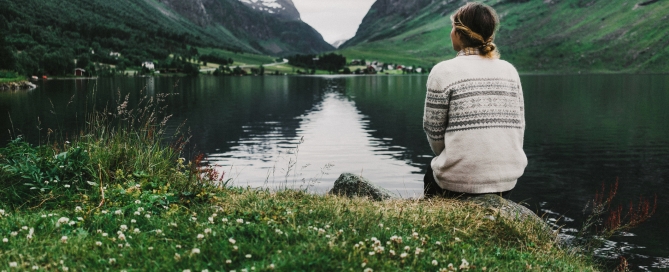 Young caucasian woman sitting near the mountain lake in Norway
