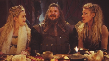 still shot of two women sitting on either side of a man at a dinner table