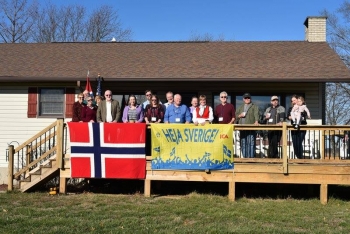 group of people standing on a deck with a Norwegian flag hanging in front