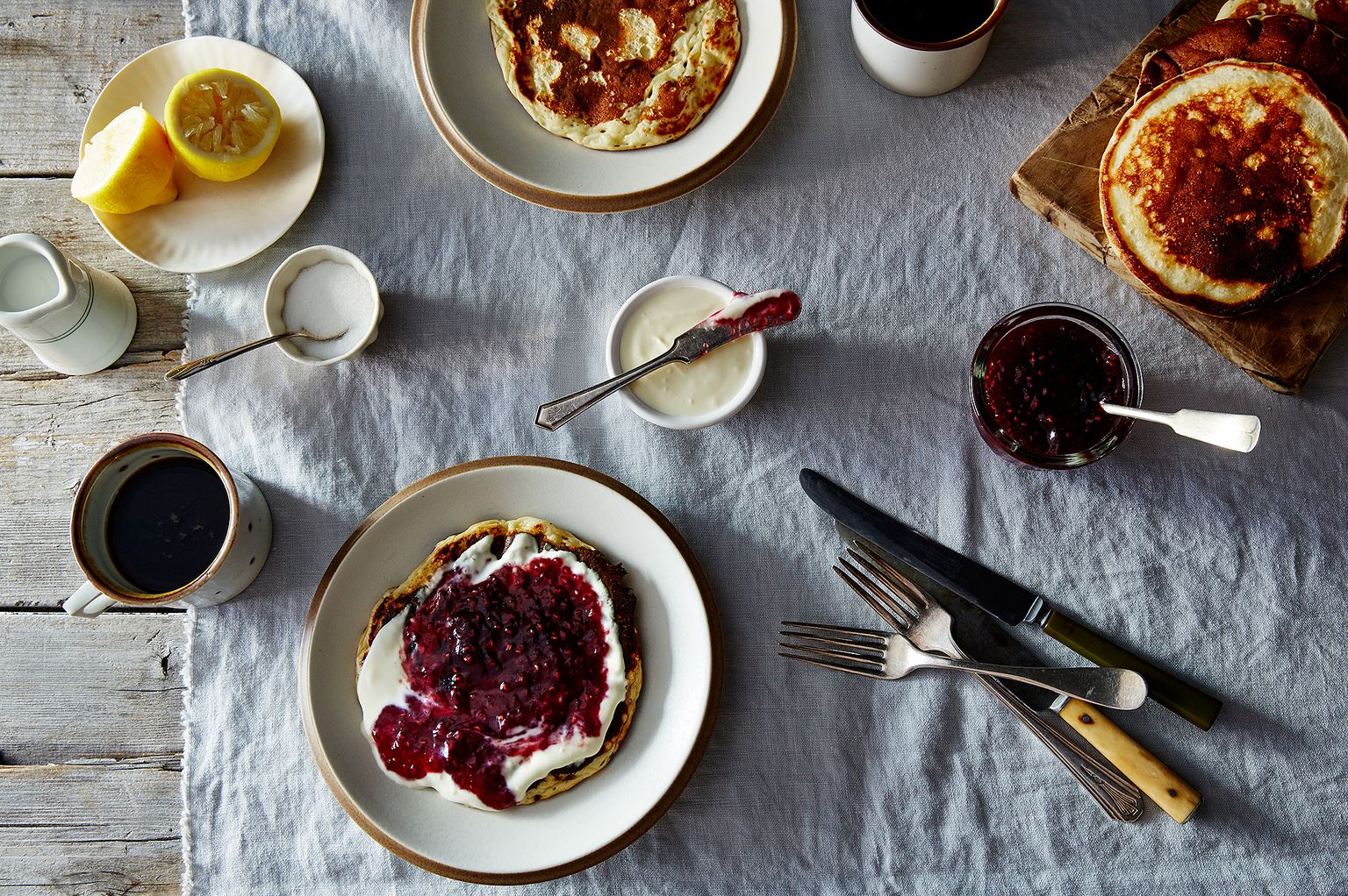table with pancakes, butter, jam, and cutlery