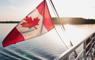 A Canada flag moving in the wind on the back of a vessel close to sunset.