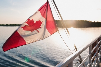 A Canada flag moving in the wind on the back of a vessel close to sunset.