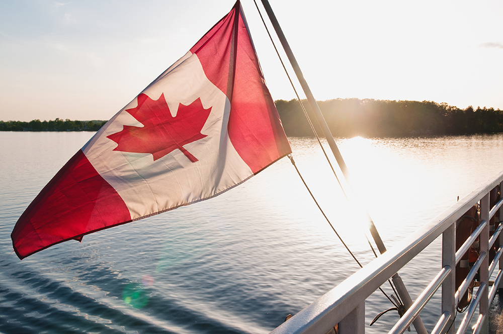 A Canada flag moving in the wind on the back of a vessel close to sunset.