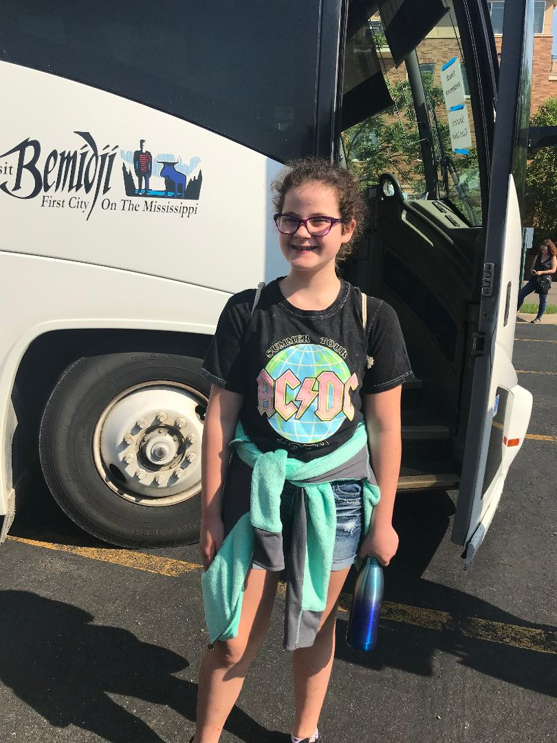 young girl with glasses, standing in front of a tour bus