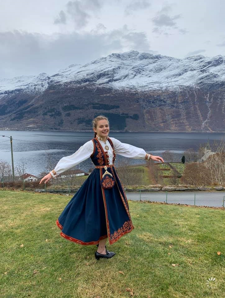 young girl in bunad dress, with fjords in the background