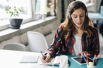 woman listening to podcast and taking notes