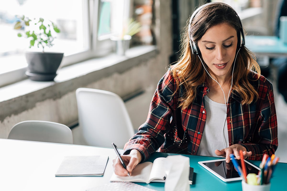 woman listening to podcast and taking notes