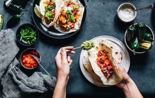 image of person preparing tacos with salsa and jalapenos