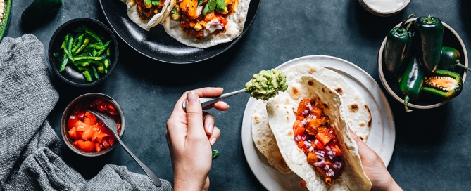image of person preparing tacos with salsa and jalapenos