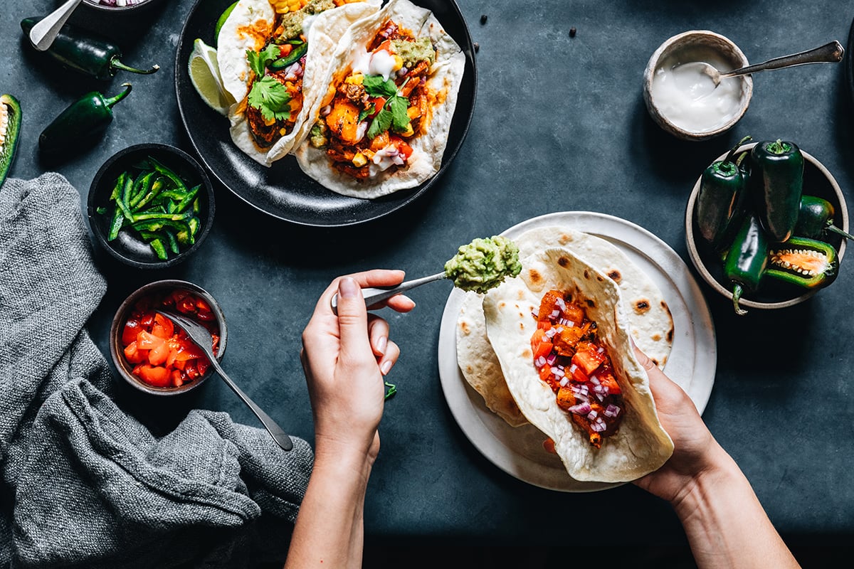 image of person preparing tacos with salsa and jalapenos